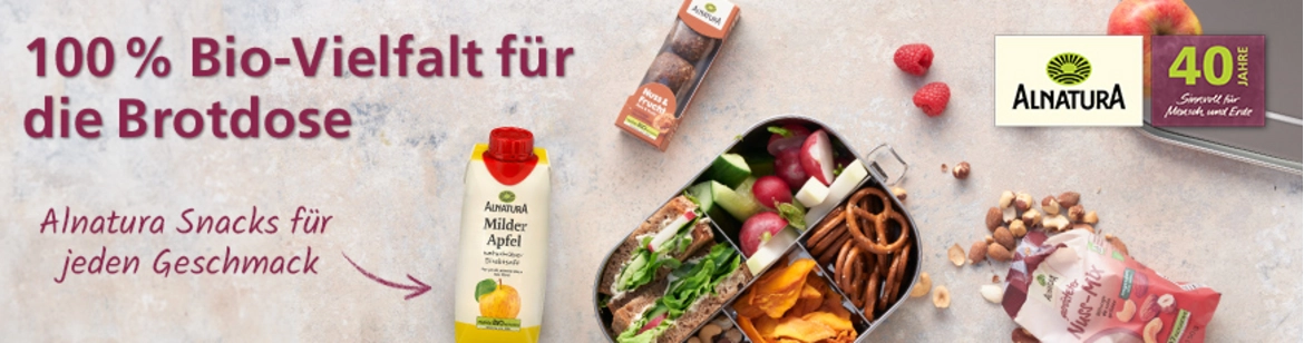 Mehrere Alnatura-Produkte auf hellem Hintergrund, in der Mitte eine Edelstahlbrotdose mit  verschiedenen Snacks und einer Banneraufschrift