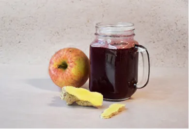 Warmer Holunder in einem Glas mit Henkel, daneben ein Apfel und aufgeschnittener Ingwer