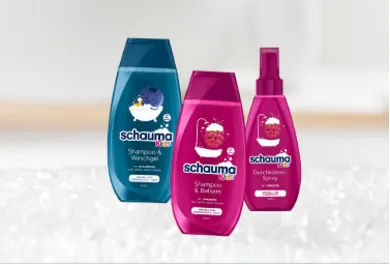 Schauma Kids Haarpflegeprodukte, drei Flaschen: Shampoo & Waschgel mit Heidelbeer-Duft, Shampoo & Balsam mit Himbeer-Duft und Durchkämm-Spray mit Kirsch-Duft. Spezielle Pflegeserie für Kinder, präsentiert vor einem weichen, verschwommenen Hintergrund.