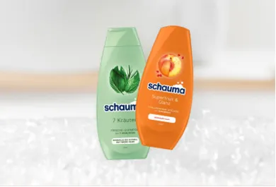 Schauma Shampoo, zwei Flaschen: 7-Kräuter Shampoo für frisches und gesundes Haar sowie Superfrucht & Glanz Shampoo mit Pfirsich-Extrakt für strahlenden Glanz. Haarpflegeprodukte, präsentiert vor einem weichen, verschwommenen Hintergrund.