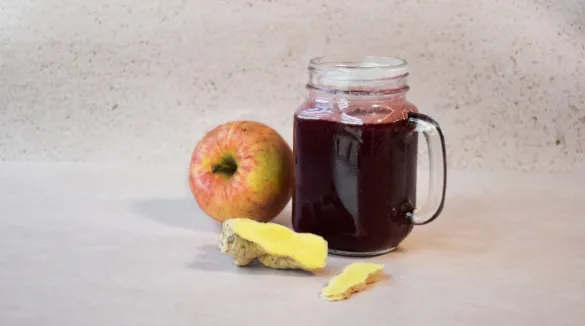 Warmer Holunder in einem Glas mit Henkel, daneben ein Apfel und aufgeschnittener Ingwer