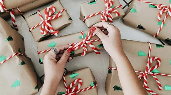 Frauenhände-roter-Nagellack-Geschenke-Geschenkpapier-mit-Weihnachtsbaumdruck-Zuckerstangen-rot-weißes-Geschenkband