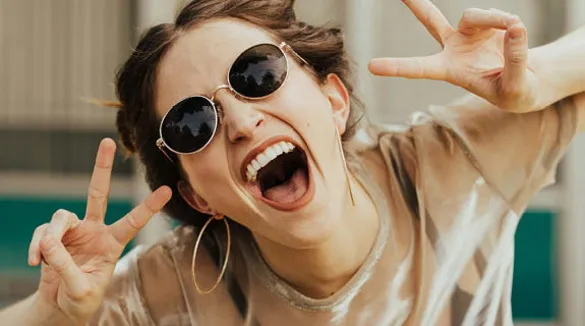 junge-Frau-Sonnenbrille-Peacezeichen-offenes-Lachen-Zähne