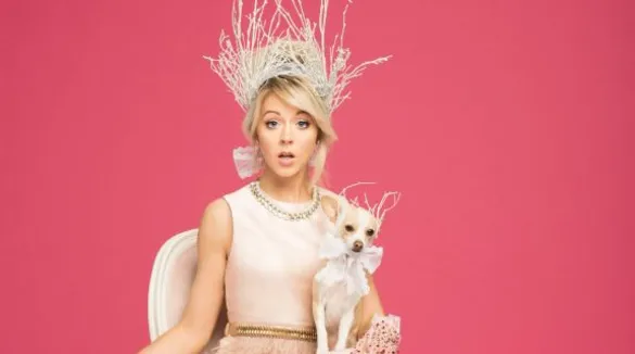 Lindsey Stirling mit einer Krone auf den Kopf, ein Hund in der Hand, Hund trägt Schleife, sehr mädchenhaft